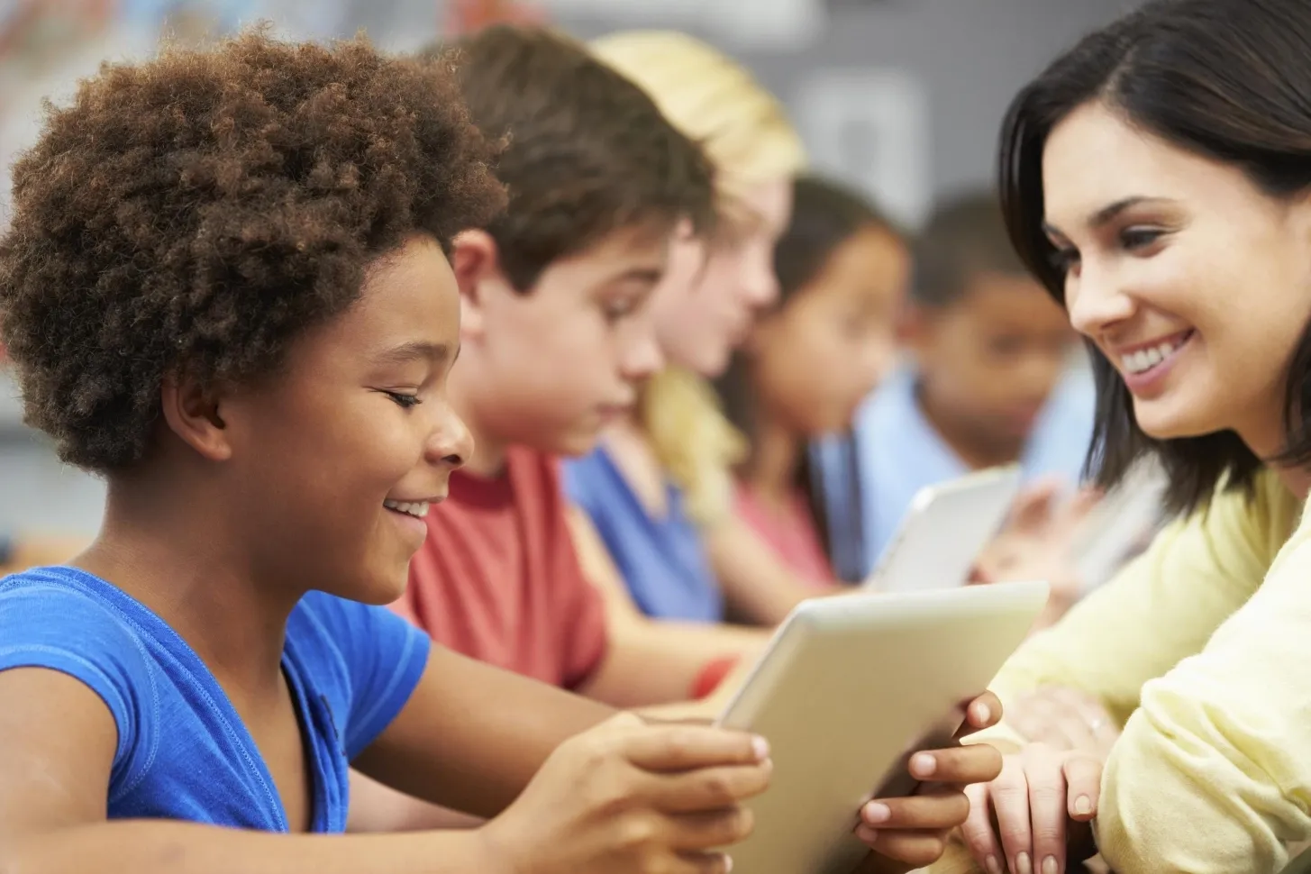 Teacher sitting with students on tablets smiling